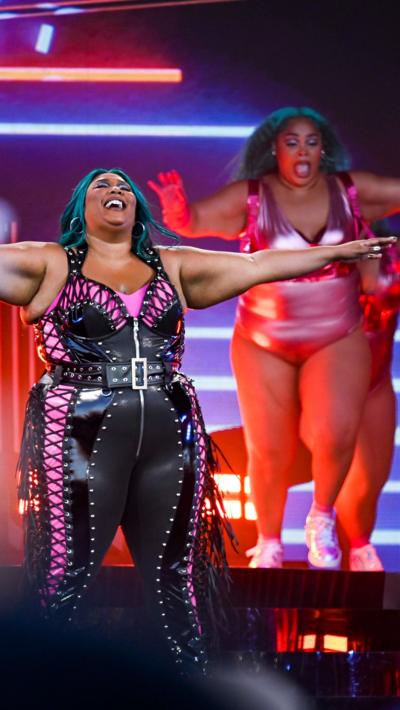 Lizzo smiles with her arms wide, wearing a black and jumpsuit at Glastonbury 2023