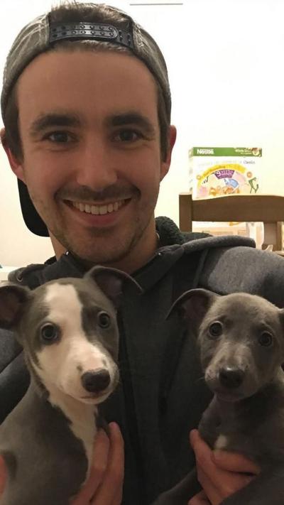 A man holding two whips. He is wearing a backwards cap and a grey hoodie.