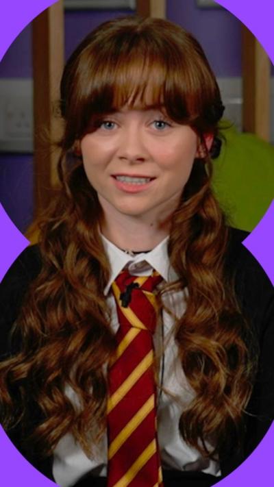 A girl with long, wavy red-brown hair and a school uniform, including a red and yellow striped tie