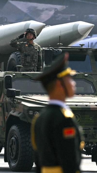 A soldier salutes on a vehicle with another in the foreground