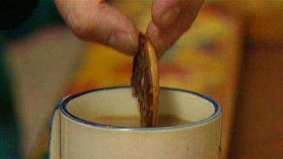 A chocolate biscuit is dunked into tea.