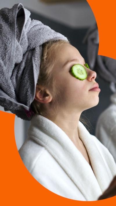 A girl in a dressing gown with cucumbers on her eyes and towel wrapped around her head, next to an adult wearing the same.