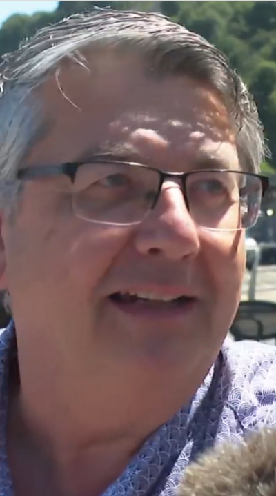 A man with white hair and glasses looks beyond the camera
