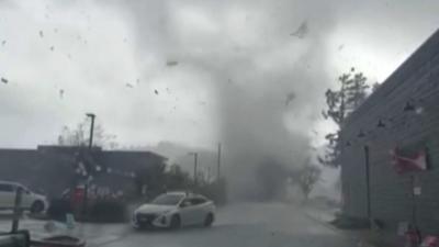 Tornado touching down in parking lot near cars and shops