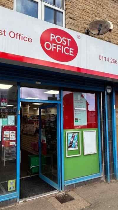 The entrance to a post office. the door is open. Above the door is a red and white sign saying Post Office.