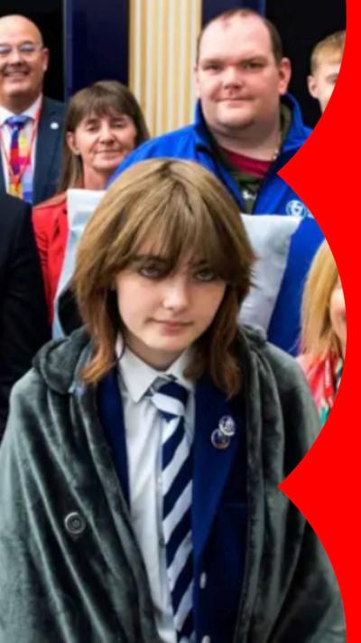 Rebecca Young has brown hair, grey blue eyes and is wearing a school uniform and a coat.