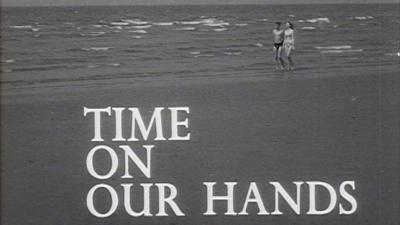 A man and woman walk along a beach. Image has 'Time on Our Hands' written on it