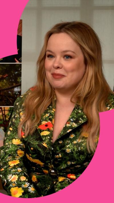 Nicola Coughlan sits and smiles. She wears a green, floral jacket. 