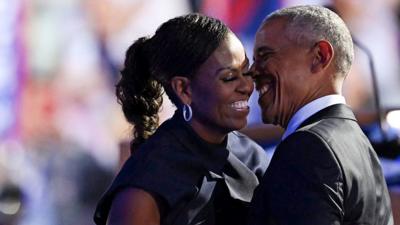 Michelle and Barack Obama laugh while embracing onstage with the audience in the background, at the DNC in Chicago on 20 August