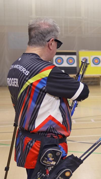 A man in sunglasses with a quiver of arrows facing some targets