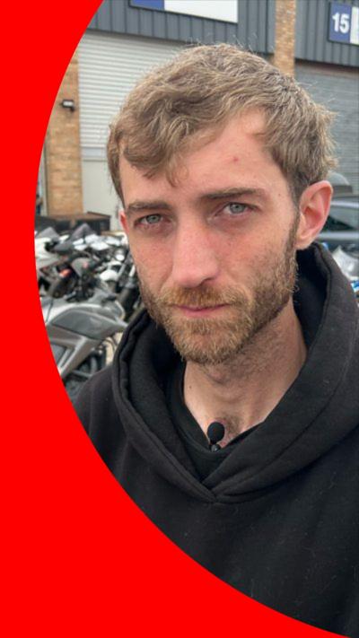 Jamie Howell has wavy frown hair, a beard and a moustache. He is a wearing a black hoodie.