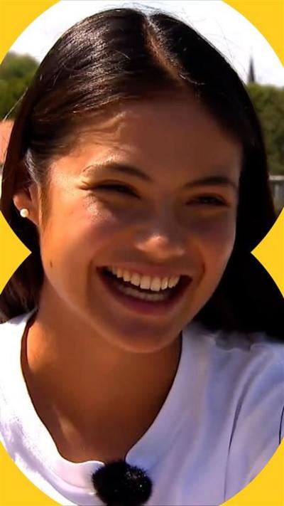 Emma Radacanu smiles. She has long brown hair and wears a white tshirt