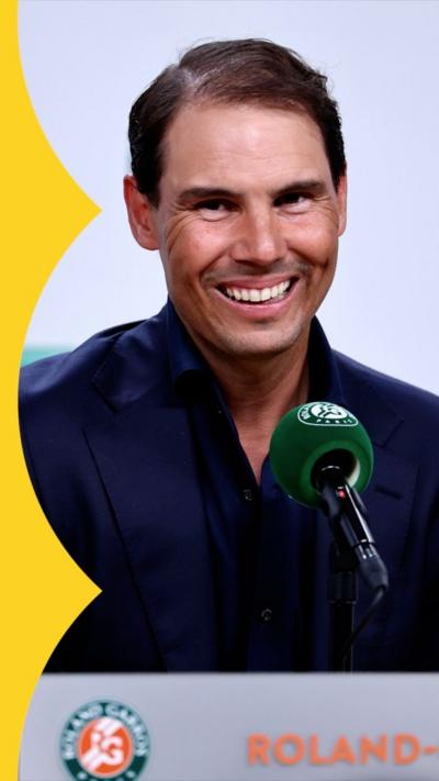 Rafa Nadal sits behind a microphone and smiles