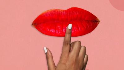 A pair of lips covered in bright red lipstick with a finger pointing at them