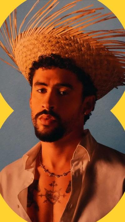 Bad Bunny has a black goatee and is wearing a straw hat and a cream shirt.