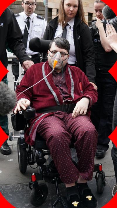 Nicholas Rossi in red silk pyjamas and an oxygen mask while being wheeled out of court.