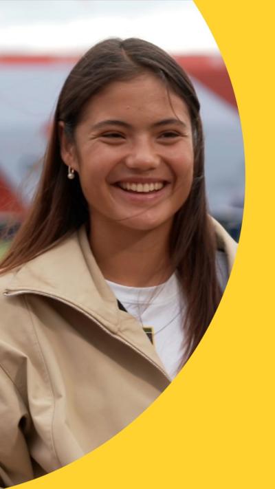 Emma Raducanu smiles at the camera. She has brown eyes and long brown hair.