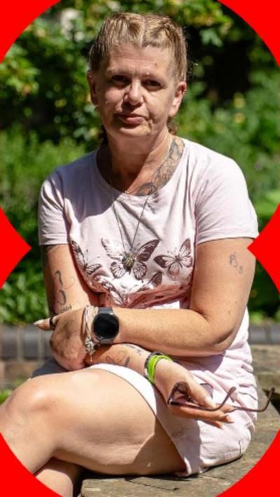 A blonde woman wearing a pink t-shirt and pink shorts sat on a ledge at the side of a pond