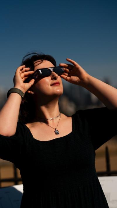 A woman wearing a black dress an special glasses looks up at the sky