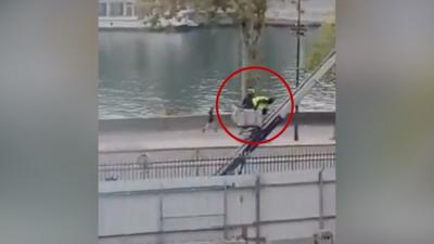 Two thieves dressed in dark clothing with one wearing a yellow hi-viz vest descend on a ladder 