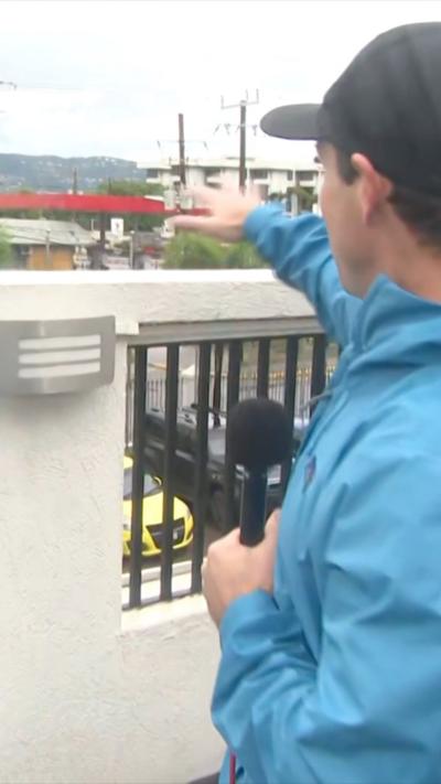 CBS reporter holding a microphone and pointing out to the sea