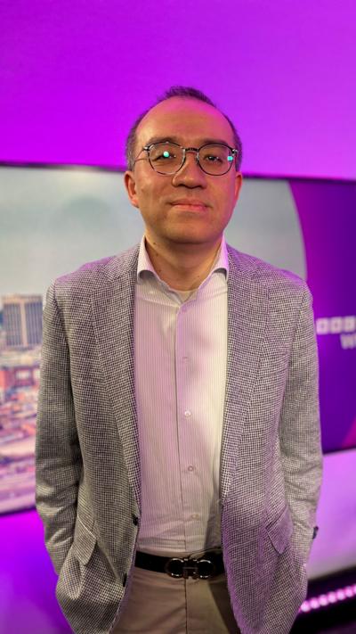 A man in glasses, grey jacket and white shirt in front of a purple background