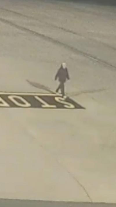 A man in a black jacket walking on an airport apron 