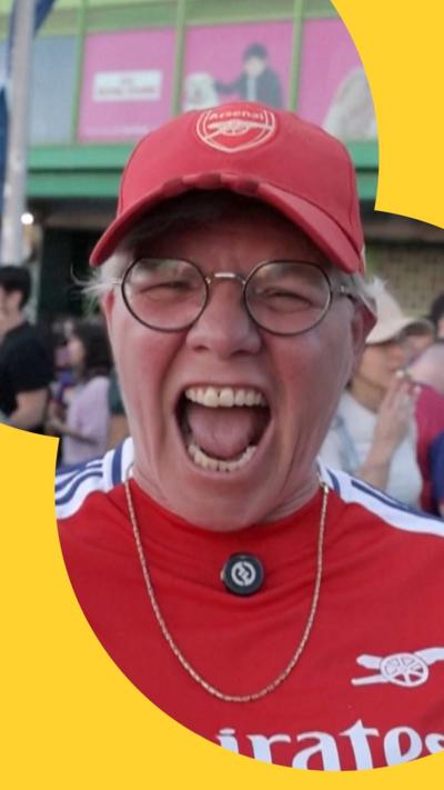 Woman screaming with delight at the camera. She is wearing a red Arsenal hat and shirt.