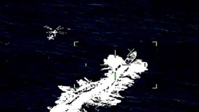 A helicopter pursues a boat in the ocean from the point of view of another helicopter's camera scope.