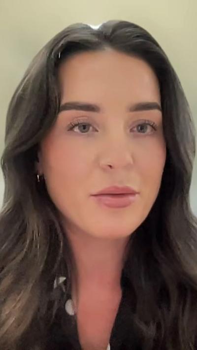 Louise Fraser, a young woman with long brown hair parted in the middle. She is facing the camera and is wearing a black top with white polka dots on it.