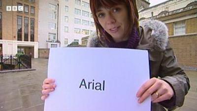 Reporter holding card with the word 'Arial' printed in a large font