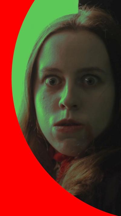 A woman wearing vampire makeup looks into the camera. Th pictures has a green hue