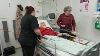 A woman in a hospital bed being tended to by nurses