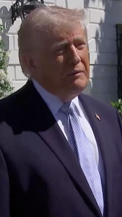 Donald Trump wears a blue suit and tie and a white shirt while listening to a reporter's question.