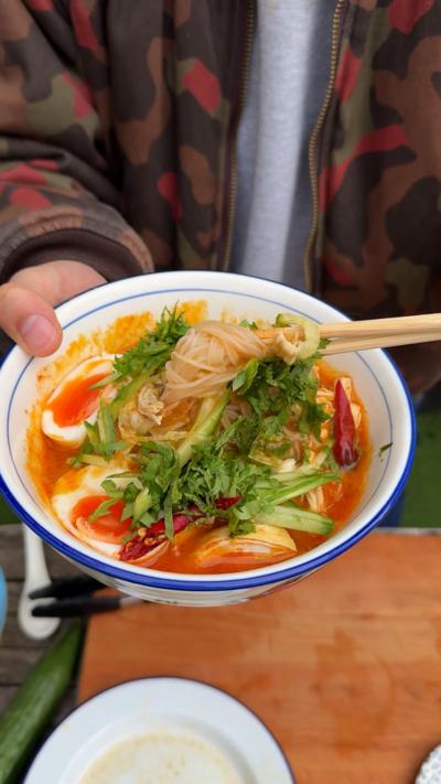 Top down view of a stone coloured bowl with chicken laksa in topped with boiled eggs, veg and lime slices