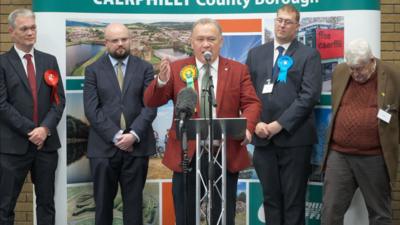 Lindsay Whittle in a red blazer on a stage with four other candidates behind him