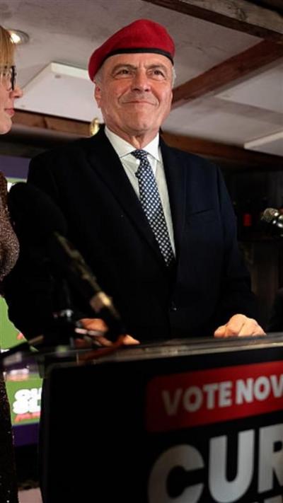 Curtis Sliwa wearing red hat and speaking at podium
