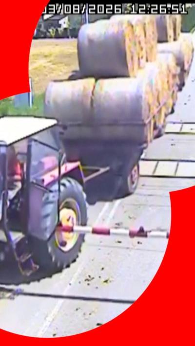 Tractor with bails of hay on a trailer crossing railway track