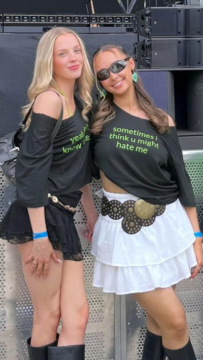A woman with long blonde hair stands beside another with tied up dark hair both are smiling toward the camera
