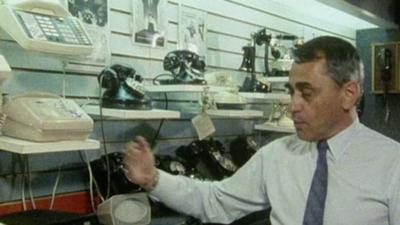 A man displays shelves of various telephone sets.