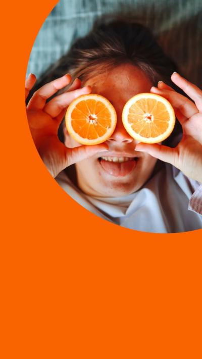 A woman lies on a bed and holds cut oranges over her eyes