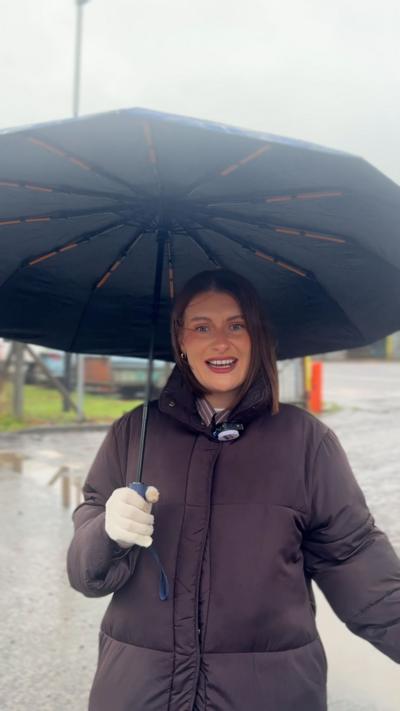 A woman with a brown jacket holding an umbrella mid talking