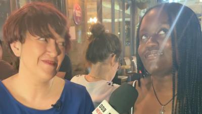 A reporter asks a question to a woman in a bar who looks indecisive