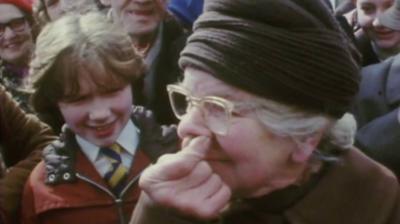 A woman sniffs some snuff in front of a crowd of people