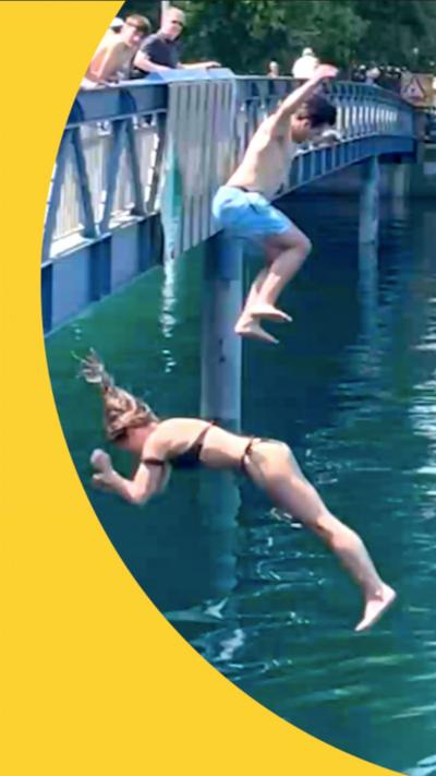 A man in swimming trunks jumps off a bridge into a clean-looking river in Switzerland as other swimmers look on