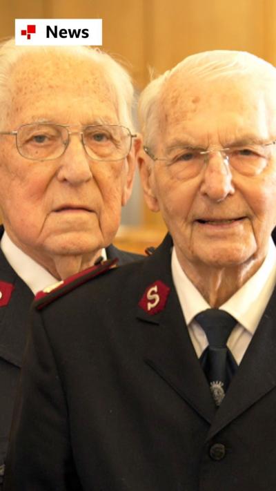 Maurice and George, both in their 90s who have been friends for 87 years. They are both older men with white hair and both are wearing a black and red branded Salvation Army uniform