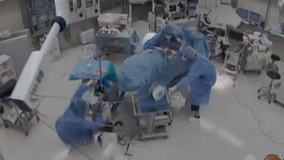CCTV image of an operating room with doctor falling over and grabbing the operating table