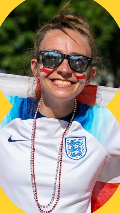 A woman in an England shirt and sunglasses smiles.