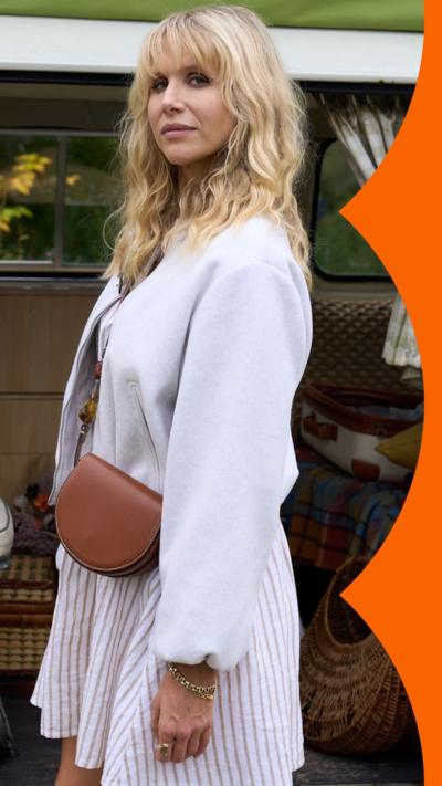 A woman with blonde hair wearing a white dress looks side-on at the camera 