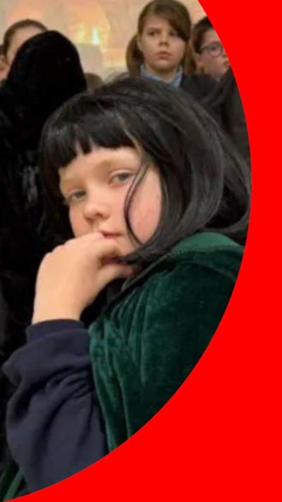 A child with a black wig on wearing a green Traitors cloak.